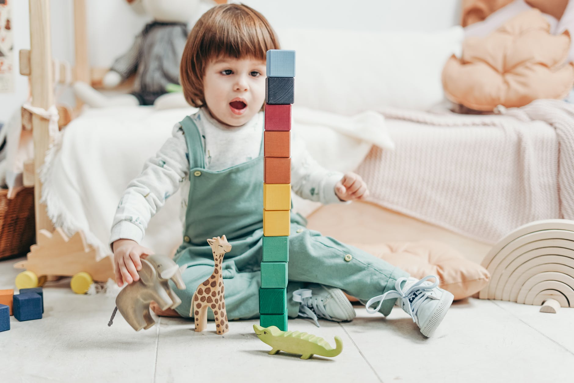 child in white long sleeve top and green dungaree trousers playing with lego blocks and toys